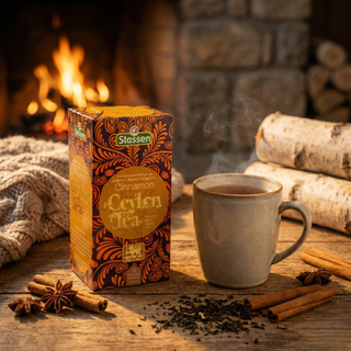 Opakowanie herbaty Stassen Cinnamon Ceylon Tea obok kubka gorącej herbaty, cynamonu i anyżu na drewnianym stole przy kominku